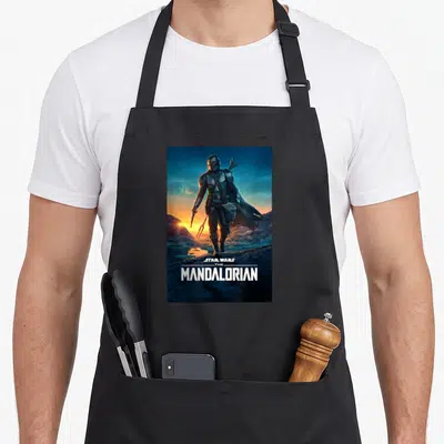Tablier de cuisine noir avec une illustration du Mandalorian de dos sur un paysage désertique au coucher de soleil.