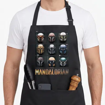Tablier de cuisine noir avec neuf casques de mercenaires disposés en grille et le titre doré The Mandalorian en bas.