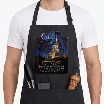 Tablier de cuisine noir avec illustration vintage Star Wars New Hope et Darth Vader en fond.