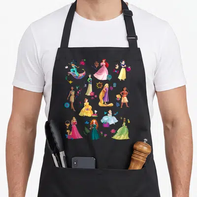 Tablier de cuisine noir avec un motif regroupant plusieurs princesses de contes de fées et leurs accessoires colorés sur fond uni.