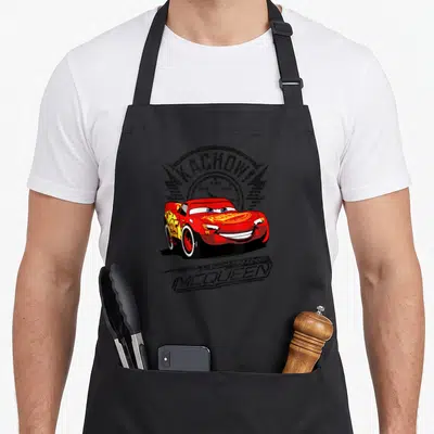 Tablier de cuisine noir avec Lightning McQueen rouge, cadran de vitesse et texte Kachow. en style vintage.