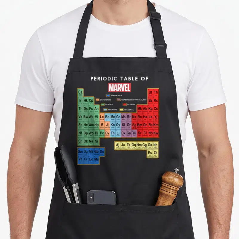Tablier de cuisine noir avec le tableau périodique des personnages Marvel coloré par catégories de héros et de vilains.