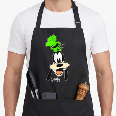 Tablier de cuisine noir avec le visage de Goofy portant une toque verte et son signature en bas.