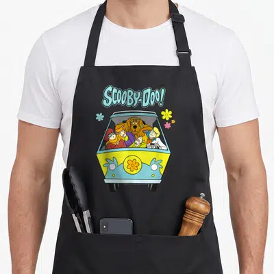 Tablier de cuisine noir avec illustration colorée de la Mystery Machine et du groupe Scooby-Doo sur fond uni.