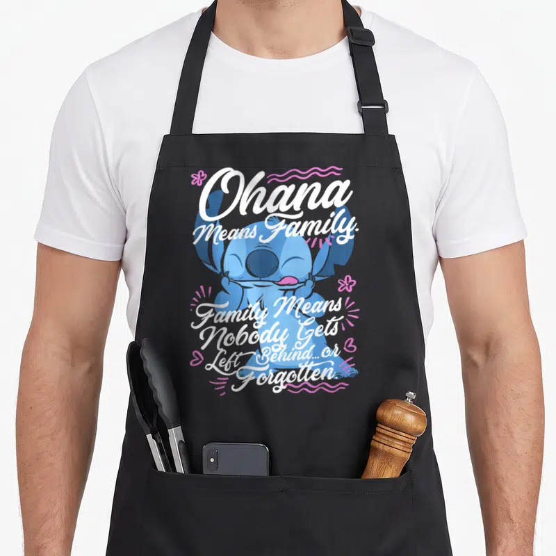 Tablier de cuisine noir avec Stitch souriant entouré du texte blanc Ohana Means Family et motifs floraux roses.