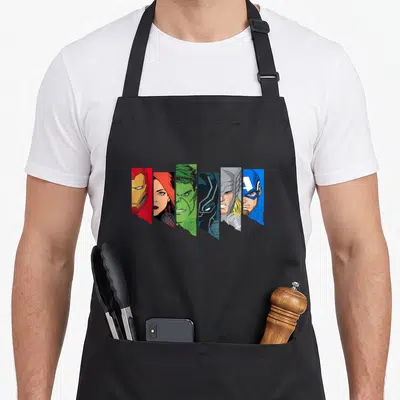 Tablier de cuisine noir avec six portraits stylisés de personnages de super-héros en bandes diagonales colorées.