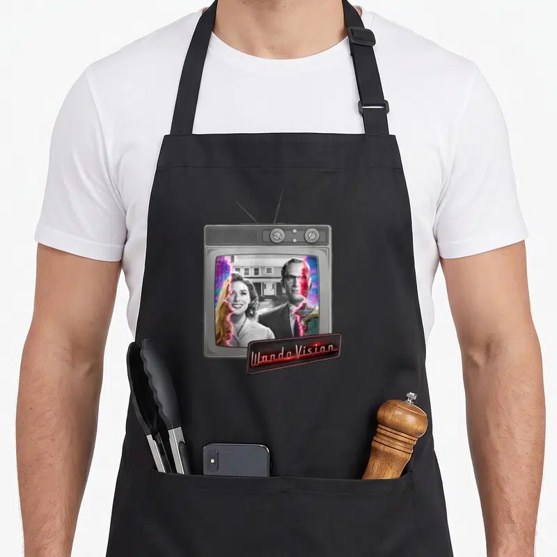 Tablier de cuisine noir avec illustration d'un téléviseur vintage affichant Wanda et Vision et leur logo en néon rouge.