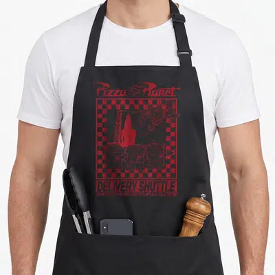 Tablier de cuisine noir avec illustration rouge Pizza Planet Delivery Shuttle, Buzz Lightyear et trois aliens souriants sur fond quadrillé.