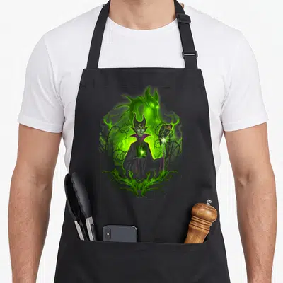 Tablier de cuisine noir avec illustration colorée de Maléfique et son corbeau sur fond de magie verte.