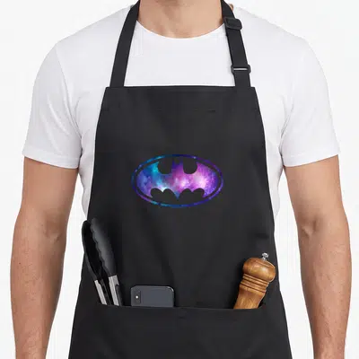 Tablier de cuisine noir avec le logo Batman rempli d'une nébuleuse spatiale aux couleurs violettes et bleues.