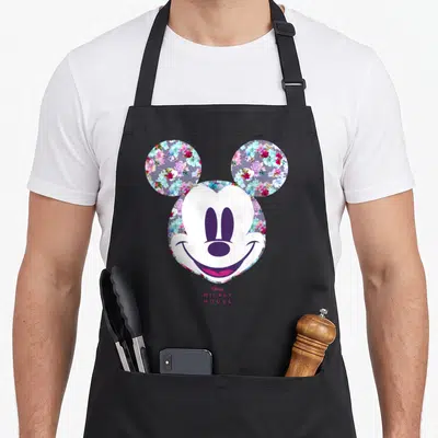 Tablier de cuisine noir avec le visage de Mickey Mouse entouré de motifs floraux colorés et du texte Disney Mickey Mouse en bas.