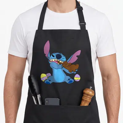 Tablier de cuisine noir avec Stitch bleu croquant un lapin de Pâques en chocolat au milieu d'œufs de couleur vive.
