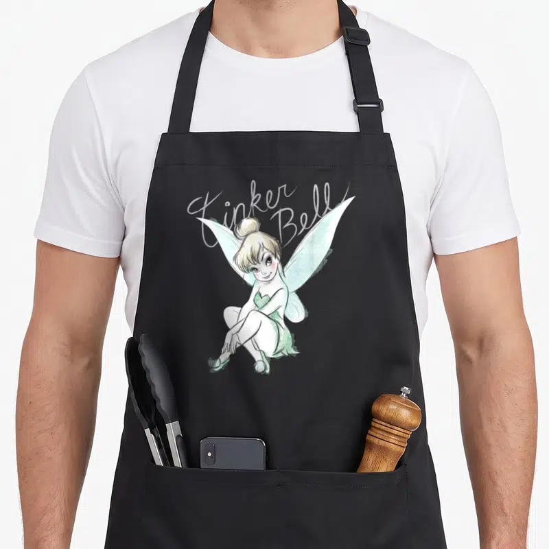 Tablier de cuisine noir avec une fée aux ailes vertes assise et le texte Tinker Bell en calligraphie blanche au-dessus.