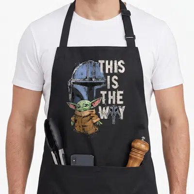 Tablier de cuisine noir avec illustration de Grogu, casque bleu et texte This Is The Way en blanc.