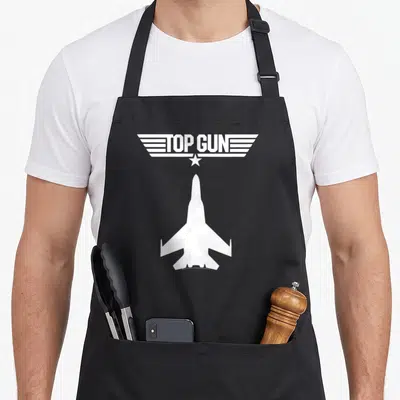 Tablier de cuisine noir avec silhouette d'avion de combat et logo Top Gun en blanc au centre.