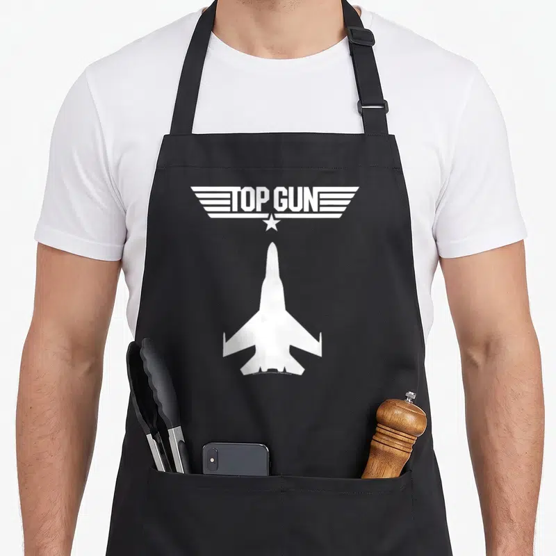 Tablier de cuisine noir avec silhouette d'avion de combat et logo Top Gun en blanc au centre.