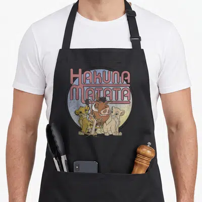 Tablier de cuisine noir avec illustration rétro de Simba, Pumbaa et Timon sous l'inscription Hakuna Matata.