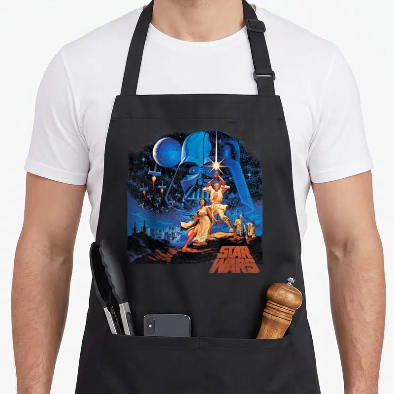 Tablier de cuisine noir avec illustration rétro de Star Wars montrant Darth Vader, Luke Skywalker, Leia, C-3PO, R2-D2 et le Death Star.