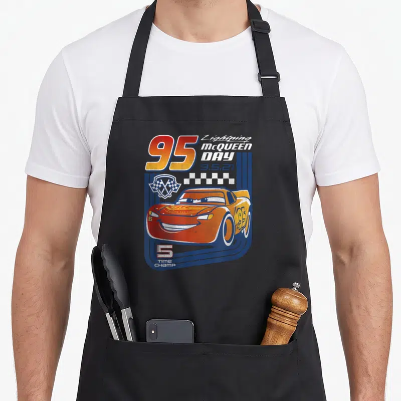 Tablier de cuisine noir avec illustration vintage de Lightning McQueen numéro 95 et drapeau à carreaux sur fond bleu.