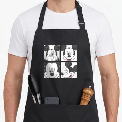 Tablier de cuisine noir avec quatre illustrations carrées de Mickey Mouse aux expressions variées en noir et blanc.