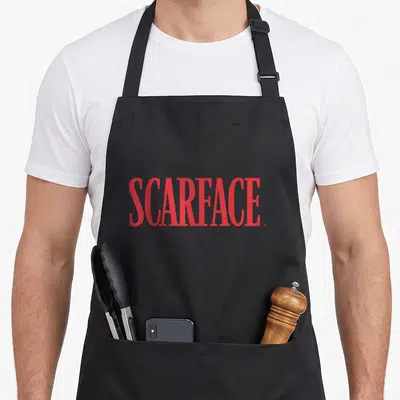 Tablier de cuisine noir avec l'inscription Scarface en grandes lettres rouges stylisées au centre du vêtement.