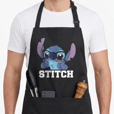 Tablier de cuisine noir avec Stitch portant des lunettes et le mot STITCH en blanc.