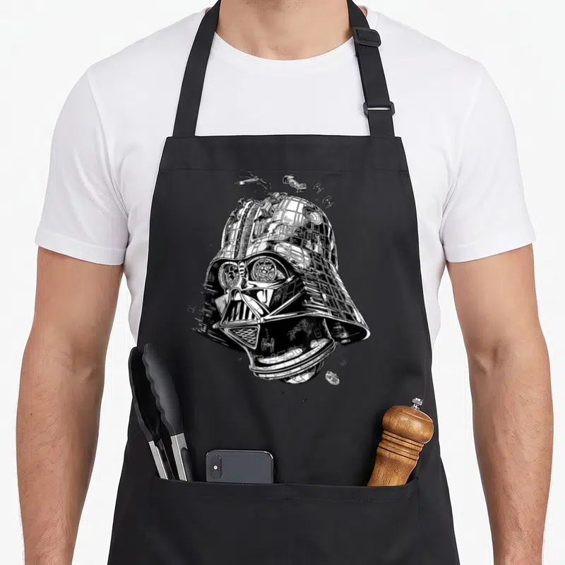 Tablier de cuisine noir avec un casque Dark Vador fusionnant à la Death Star et des vaisseaux en dessin noir et blanc.