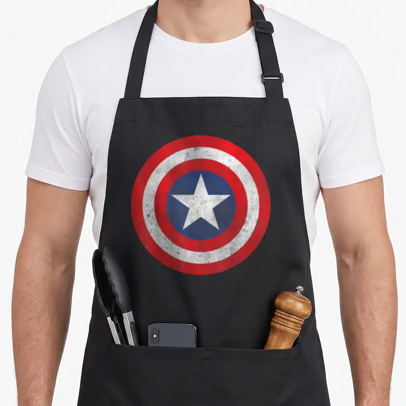 Tablier de cuisine noir avec écusson Captain America aux couleurs rouges, blanches et bleues en style vintage.