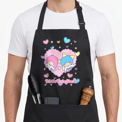 Tablier de cuisine noir avec illustration Little Twin Stars dans un coeur rose entouré d'étoiles et de petits coeurs colorés.