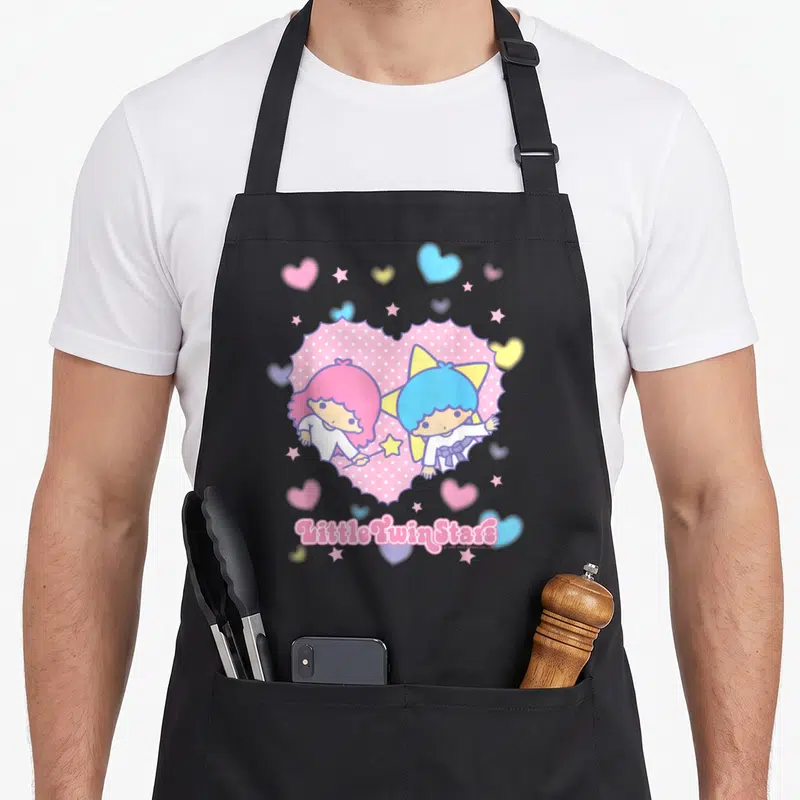 Tablier de cuisine noir avec illustration Little Twin Stars dans un coeur rose entouré d'étoiles et de petits coeurs colorés.