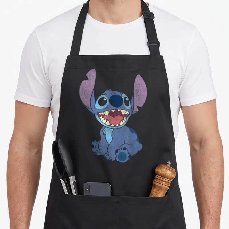 Tablier de cuisine noir avec illustration de Stitch assis affichant un large sourire joyeux et des dents pointues.