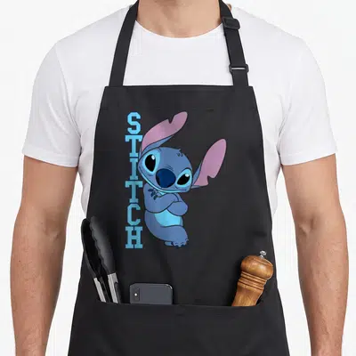 Tablier de cuisine noir avec Stitch posant les bras croisés et le texte STITCH vertical en bleu clair.