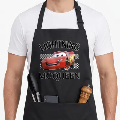 Tablier de cuisine noir avec illustration de Lightning McQueen Finish entouré de damiers et texte noir.