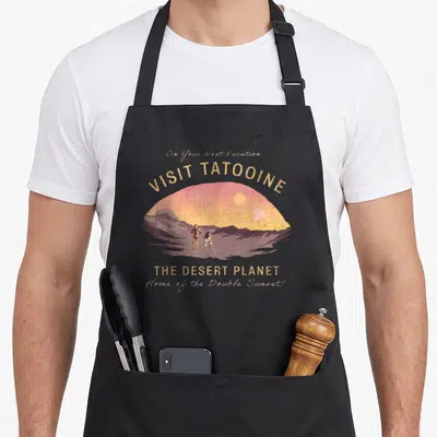 Tablier de cuisine noir avec illustration vintage de Tatooine, double soleil et personnages en silhouette.