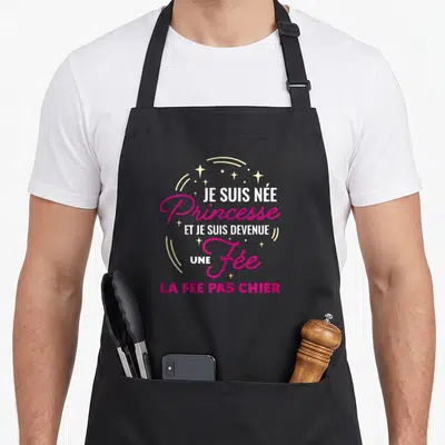 Tablier de cuisine noir avec l'inscription Je suis née Princesse et je suis devenue une Fée la fée pas chier entourée d'étoiles dorées.
