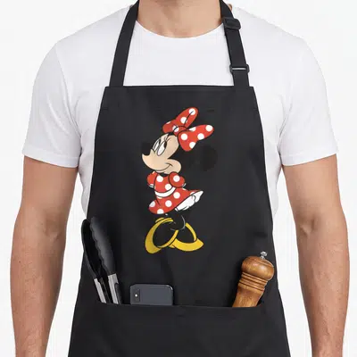 Tablier de cuisine noir avec illustration de Minnie Mouse en robe rouge à pois blancs et grand nœud assorti sur la tête.