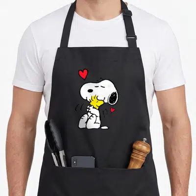 Tablier de cuisine noir avec Snoopy embrassant Woodstock entouré de deux petits cœurs rouges.