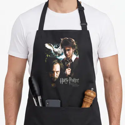 Tablier de cuisine noir avec illustration d'Harry Potter tenant une baguette, le visage de Sirius Black et l'hibou Hedwige en vol.