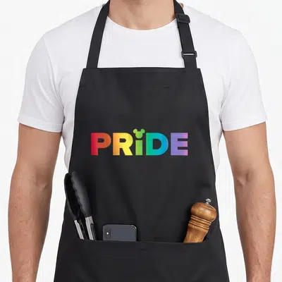 Tablier de cuisine noir avec linscription PRIDE en dégradé arc-en-ciel et silhouettes doreilles Mickey au-dessus du point i.