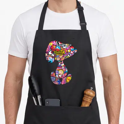 Tablier de cuisine noir avec une grande silhouette Snoopy composée de vignettes Peanuts multicolores et de textes comme I SNOOPY et POW.