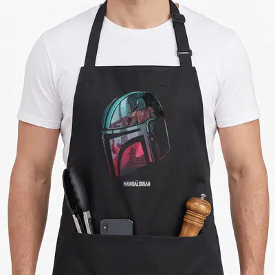 Tablier de cuisine noir avec illustration colorée du casque du Mandalorian et texte blanc en bas.