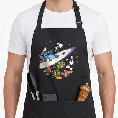 Tablier de cuisine noir avec Stitch sur une planche à voile entouré de fleurs tropicales et palmiers blancs.