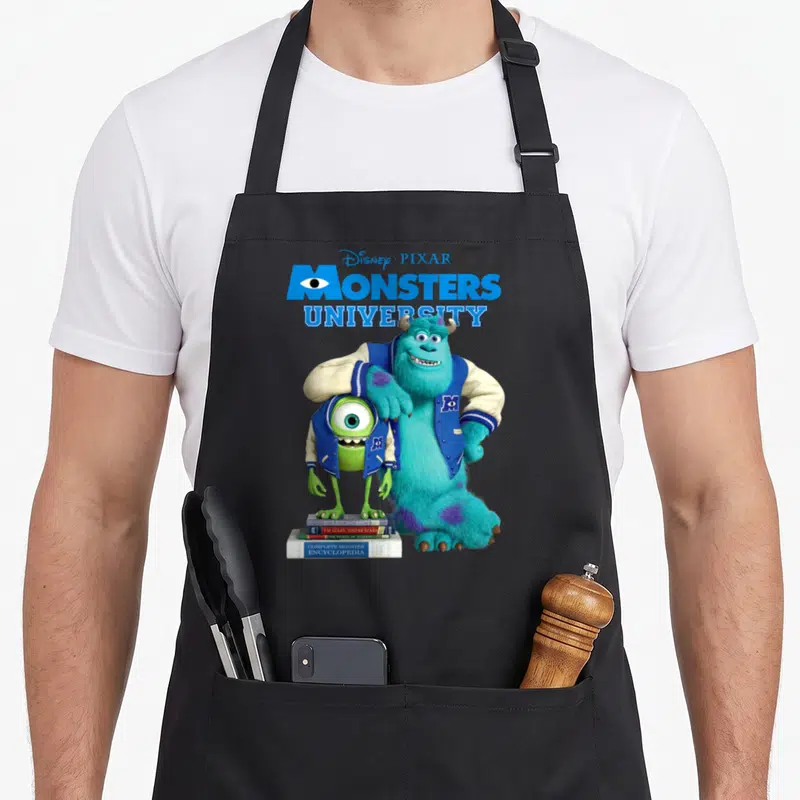 Tablier de cuisine noir avec Mike et Sulley en blouson bleu posant sur des livres de monstres.