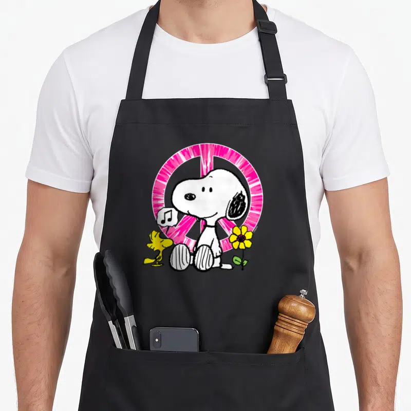 Tablier de cuisine noir avec Snoopy, Woodstock, une note de musique et un panneau de paix rose vif.