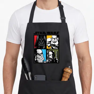Tablier de cuisine noir avec illustration colorée de Darth Vader, Stormtroopers et Boba Fett au logo Star Wars en haut.