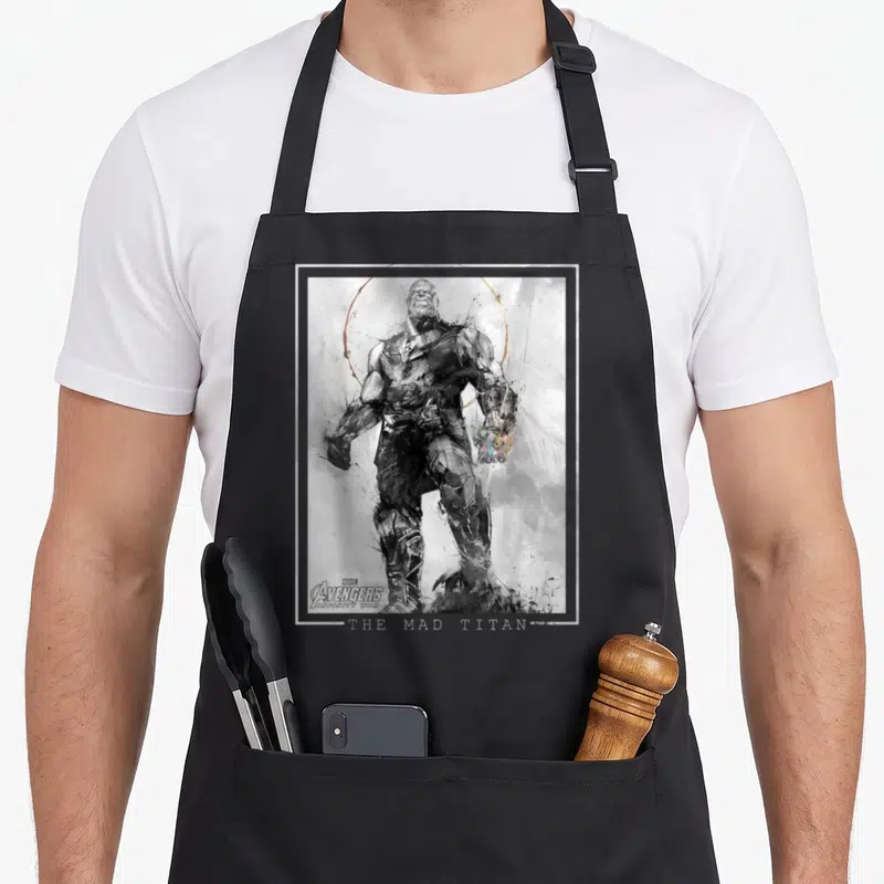 Tablier de cuisine noir avec un croquis artistique de Thanos le Mad Titan tenant la Gant de l'Infini colorée sur fond gris texturé.