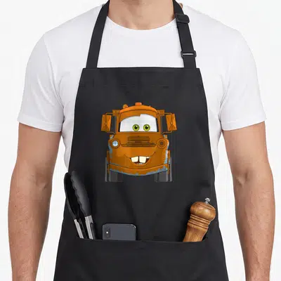 Tablier de cuisine noir avec illustration frontale du camion orange Mater aux yeux verts et sourire expressif.