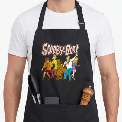 Tablier de cuisine noir avec le logo Scooby-Doo en rose et le groupe dans des tenues colorées sur fond uni.