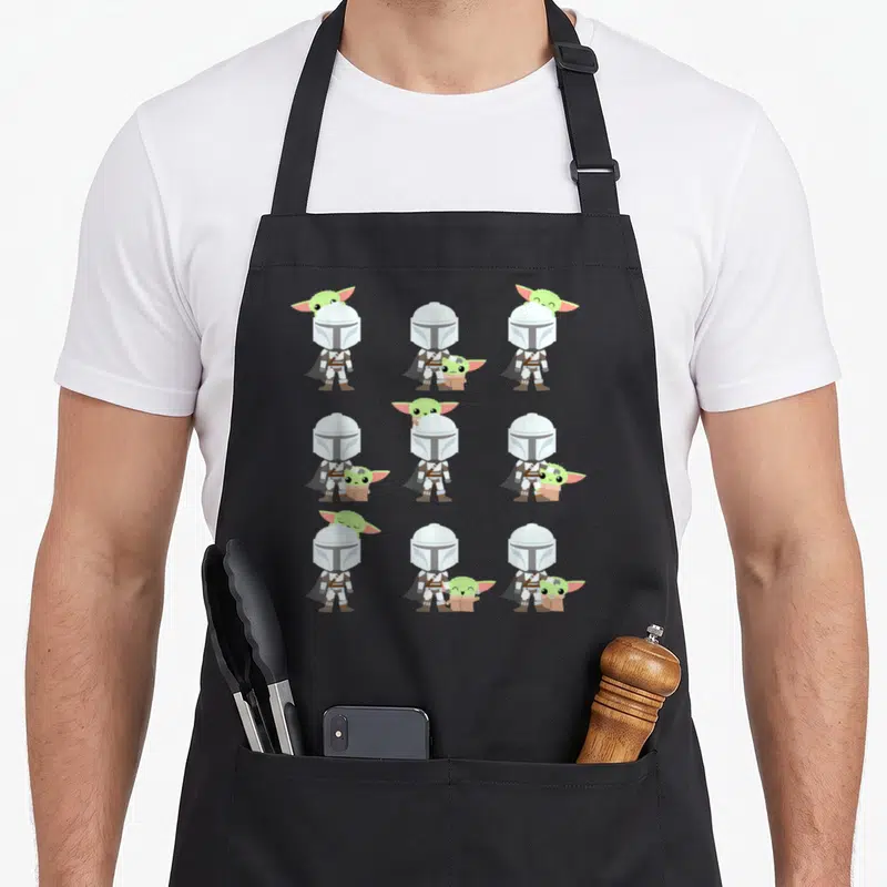 Tablier de cuisine noir avec neuf illustrations du Mandalorian et Grogu en version chibi aux expressions variées et adorables.
