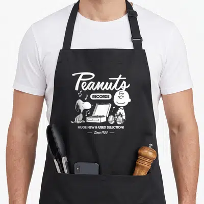 Tablier de cuisine noir avec illustration blanche Snoopy, Charlie Brown et texte Peanuts Records Since 1950.